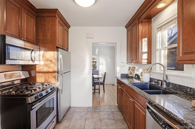 kitchen featuring dark stone countertops, brown cabinets, appliances with stainless steel finishes, and a sink