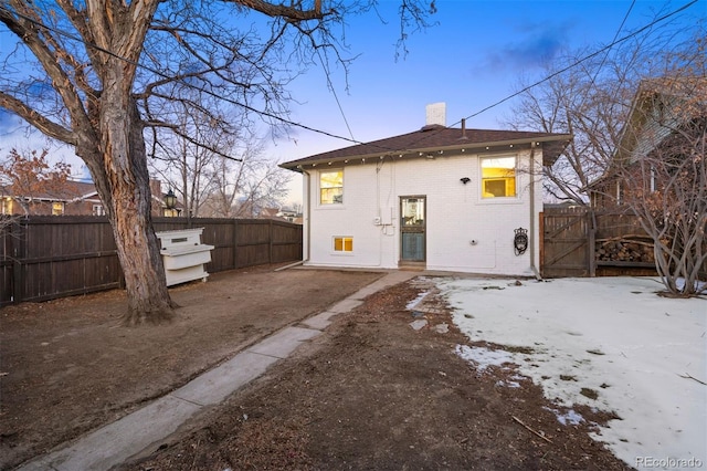 rear view of property featuring brick siding, a chimney, and fence