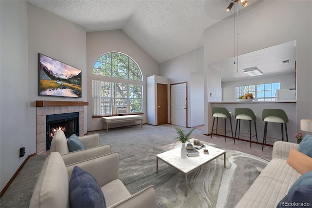 living room featuring light carpet, a textured ceiling, a tiled fireplace, and high vaulted ceiling