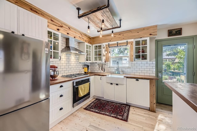 2844 Bellaire St, Denver, CO 80207 - kitchen with stainless steel appliances, wood counters, wall chimney exhaust hood, a sink, and backsplash