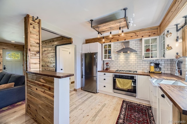 2844 Bellaire St, Denver, CO 80207 - kitchen with wooden counters, appliances with stainless steel finishes, wall chimney exhaust hood, glass insert cabinets, and decorative backsplash
