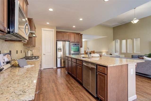 kitchen featuring light stone counters, open floor plan, dark wood-style floors, decorative backsplash, and appliances with stainless steel finishes