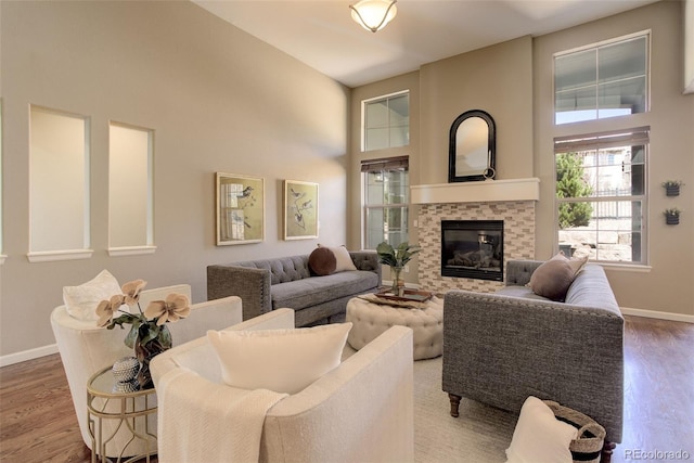 living room featuring baseboards, a towering ceiling, a glass covered fireplace, and wood finished floors