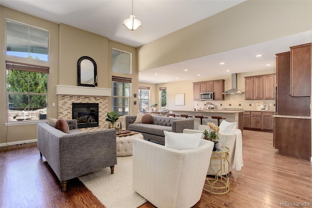 living area featuring a glass covered fireplace, baseboards, recessed lighting, a high ceiling, and wood finished floors