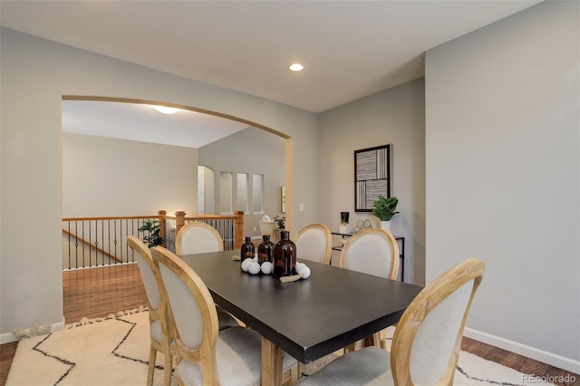 dining space with baseboards, recessed lighting, arched walkways, and wood finished floors