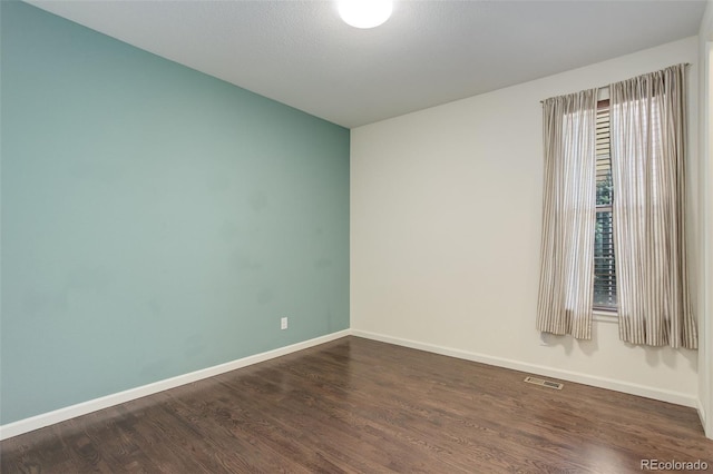 unfurnished room with visible vents, baseboards, and dark wood finished floors