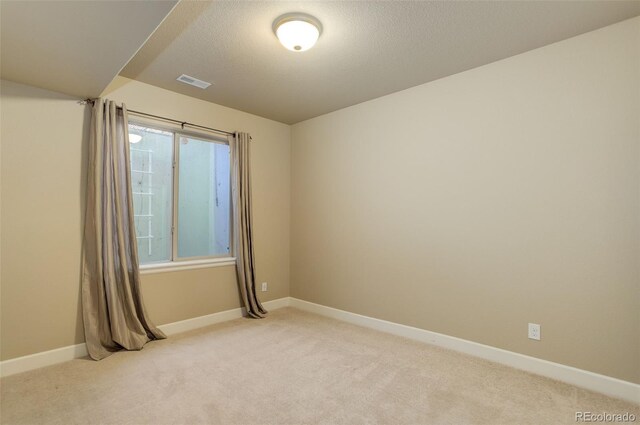 unfurnished room with a textured ceiling, light colored carpet, baseboards, and visible vents