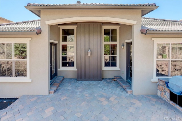 view of exterior entry featuring a patio area, stucco siding, a tiled roof, and board and batten siding
