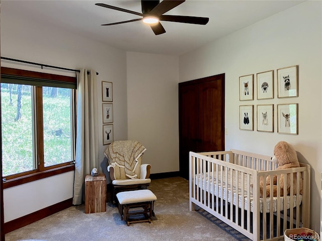 bedroom featuring a nursery area, carpet floors, and ceiling fan