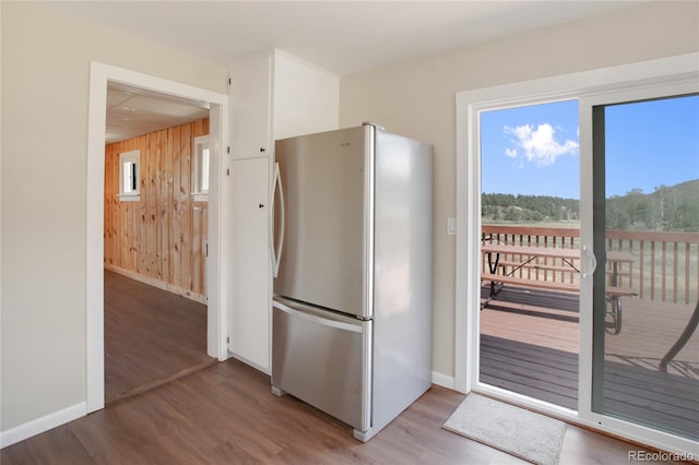 kitchen featuring stainless steel refrigerator, hardwood / wood-style flooring, and wooden walls