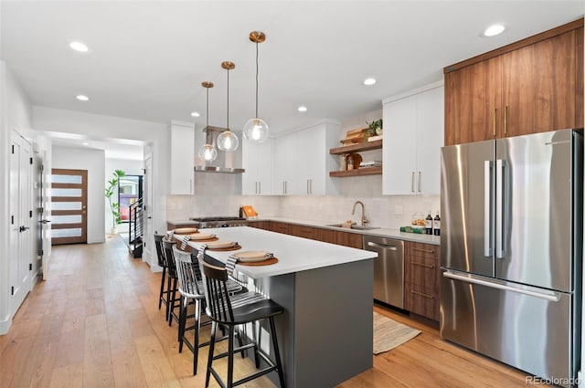 kitchen with light wood-type flooring, stainless steel appliances, decorative light fixtures, a center island, and white cabinetry