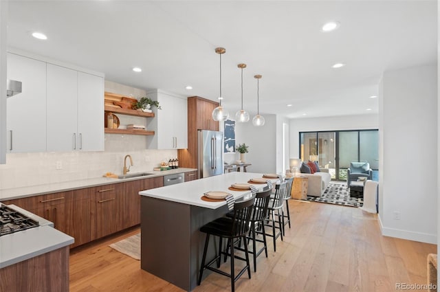 kitchen with white cabinetry, sink, stainless steel appliances, hanging light fixtures, and light hardwood / wood-style flooring