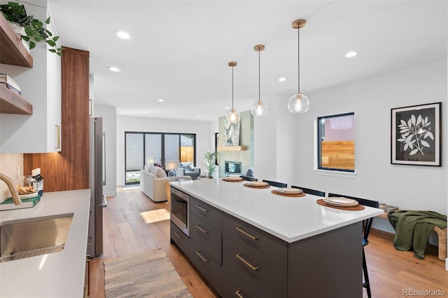 kitchen featuring sink, a fireplace, pendant lighting, and light wood-type flooring