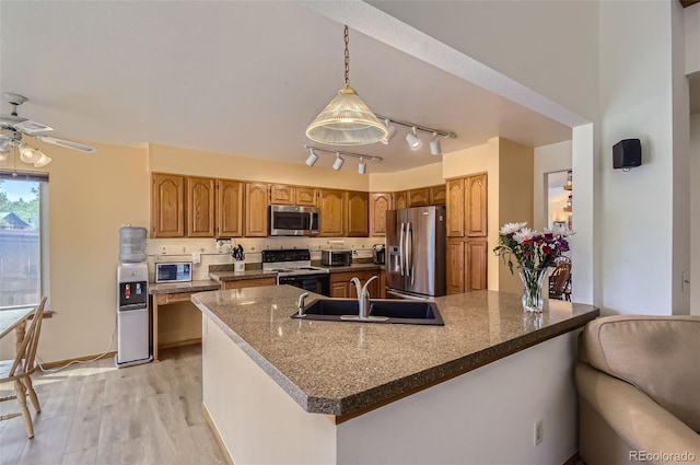 kitchen featuring ceiling fan, brown cabinets, a sink, stainless steel appliances, and light wood-style flooring