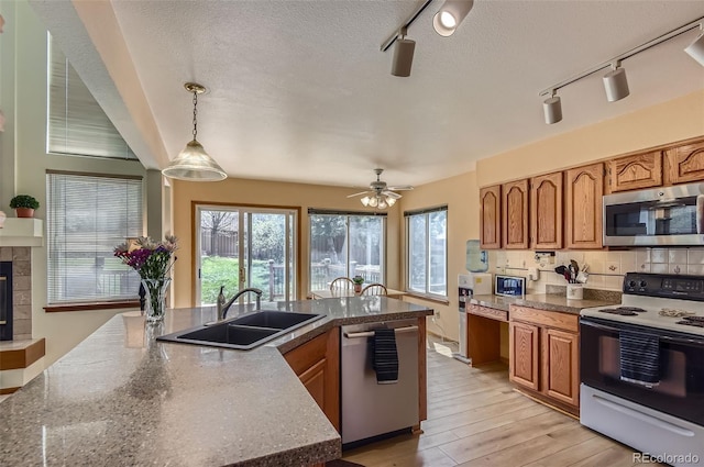 kitchen with track lighting, appliances with stainless steel finishes, brown cabinetry, and a sink