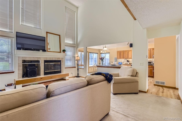 living room featuring visible vents, a tiled fireplace, high vaulted ceiling, baseboards, and light carpet