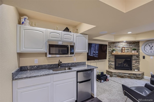 kitchen featuring a sink, a fireplace, stainless steel appliances, and white cabinetry