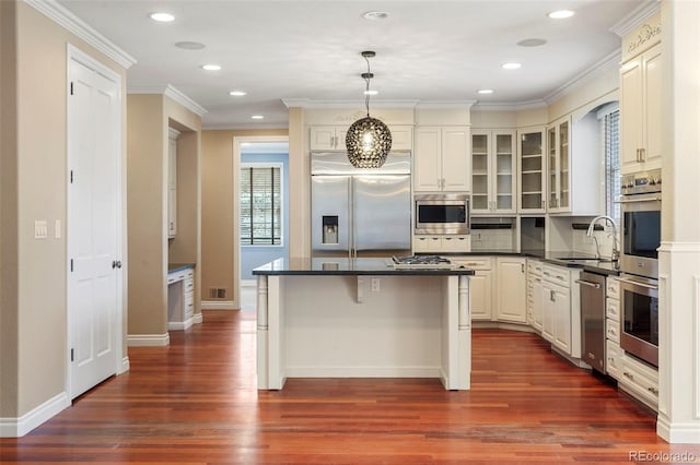 kitchen featuring a kitchen island, a sink, glass insert cabinets, built in appliances, and dark countertops