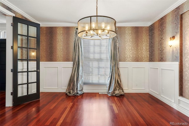 unfurnished dining area featuring a wainscoted wall, ornamental molding, dark wood finished floors, wallpapered walls, and a chandelier