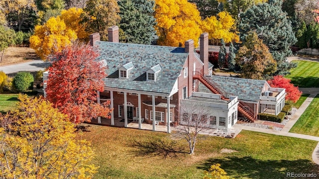 back of house featuring brick siding, a high end roof, a lawn, and stairs