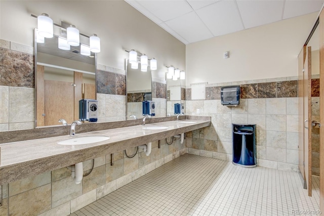 bathroom featuring tile patterned flooring, tile walls, and dual sinks