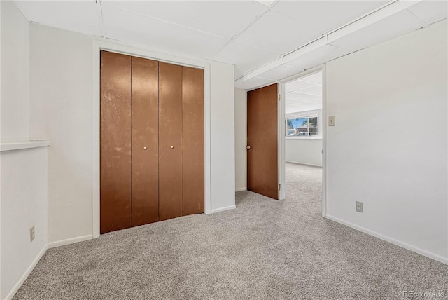 unfurnished bedroom with a drop ceiling, a closet, and light carpet