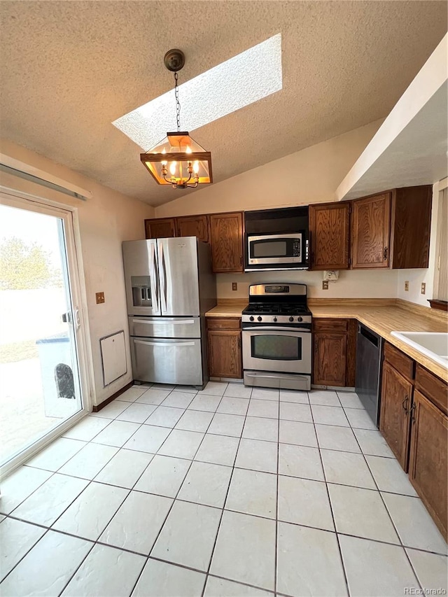 kitchen with appliances with stainless steel finishes, a textured ceiling, lofted ceiling with skylight, and hanging light fixtures