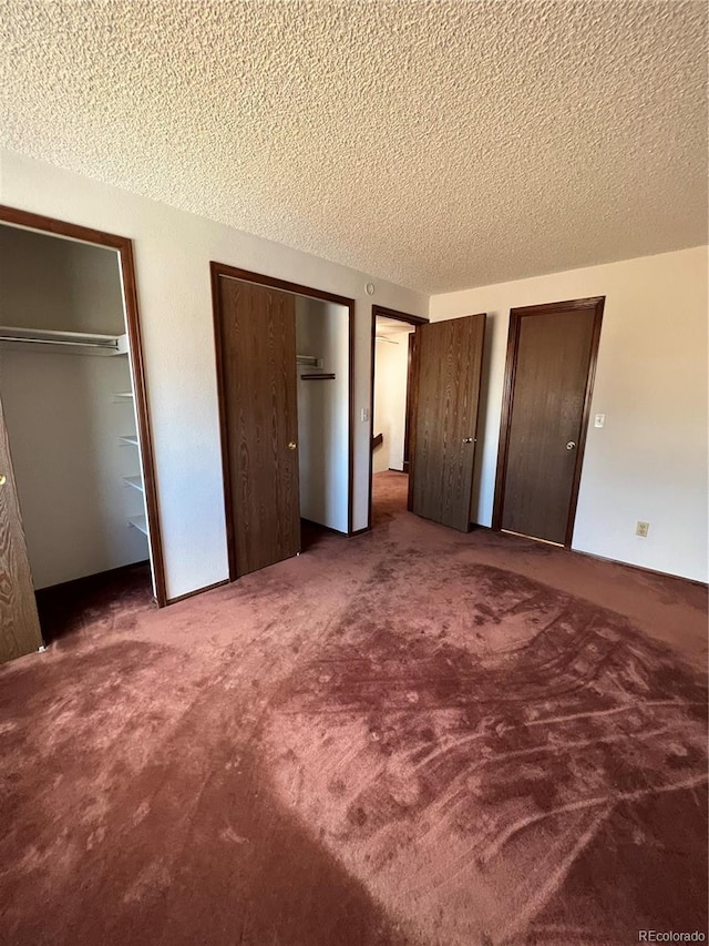 unfurnished bedroom with a textured ceiling, dark carpet, and multiple closets