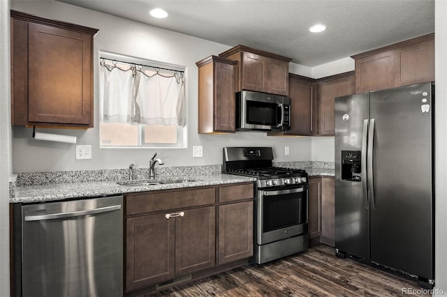 7568 Benecia Dr, Fountain, CO 80817 - kitchen featuring appliances with stainless steel finishes, a sink, dark wood finished floors, light stone countertops, and dark brown cabinets