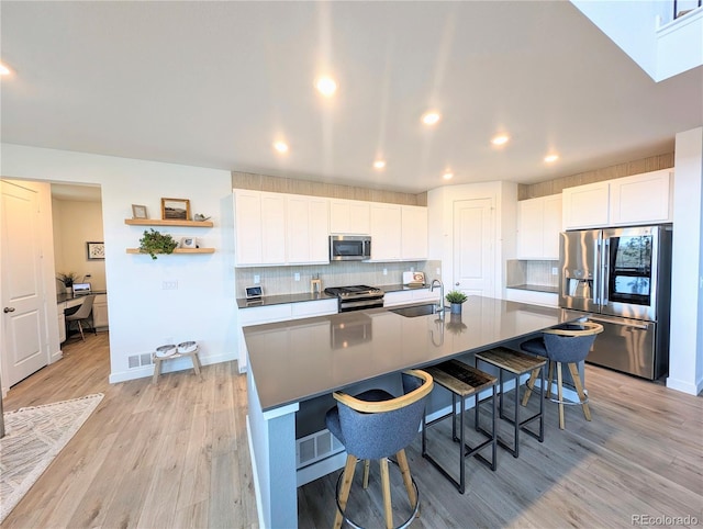 864 Clover Loop, Erie, CO 80026 - kitchen featuring appliances with stainless steel finishes, a breakfast bar area, light wood-style flooring, decorative backsplash, and white cabinets
