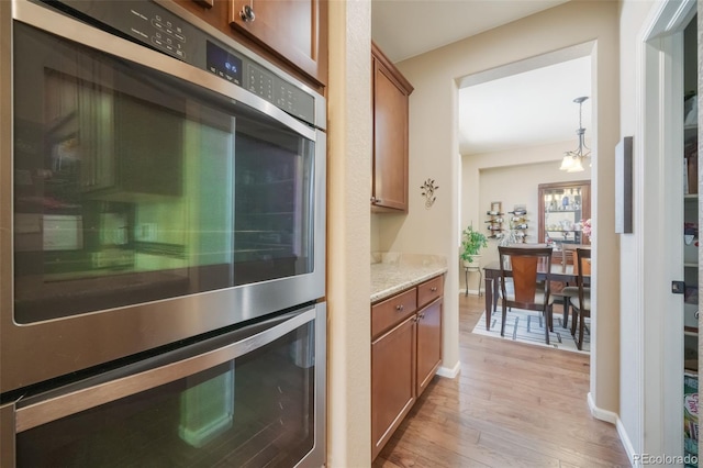 kitchen featuring hanging light fixtures, double oven, light hardwood / wood-style floors, light stone counters, and a chandelier