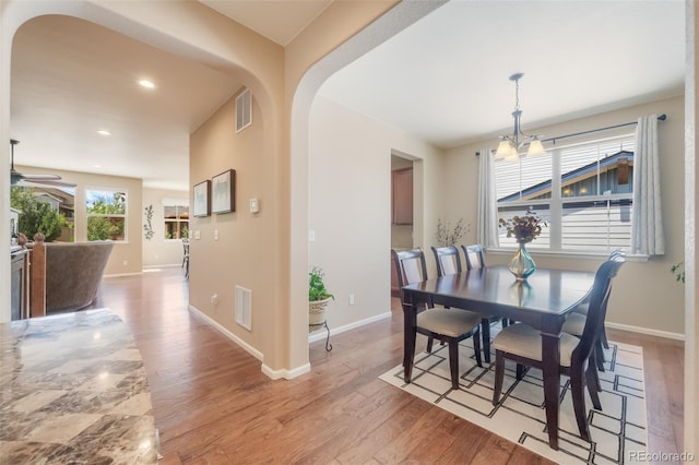 dining area with ceiling fan with notable chandelier and light hardwood / wood-style floors