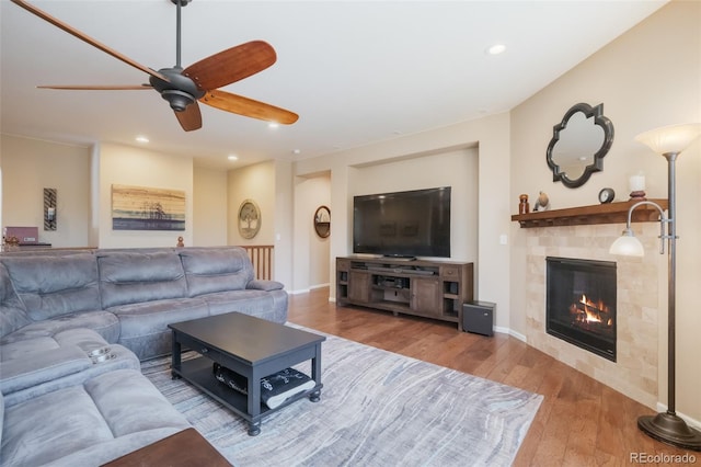 living room featuring a tiled fireplace, ceiling fan, and hardwood / wood-style floors