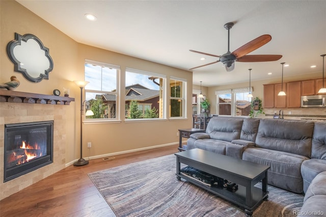 living room featuring ceiling fan, a tiled fireplace, a wealth of natural light, and light hardwood / wood-style flooring