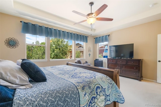 carpeted bedroom with ceiling fan and a raised ceiling