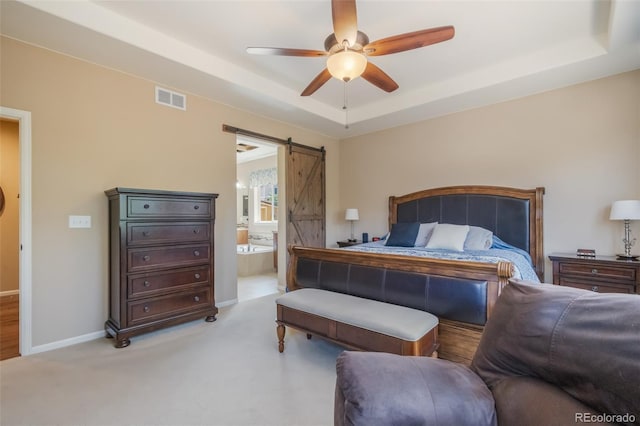 carpeted bedroom with a barn door, a raised ceiling, ceiling fan, and connected bathroom