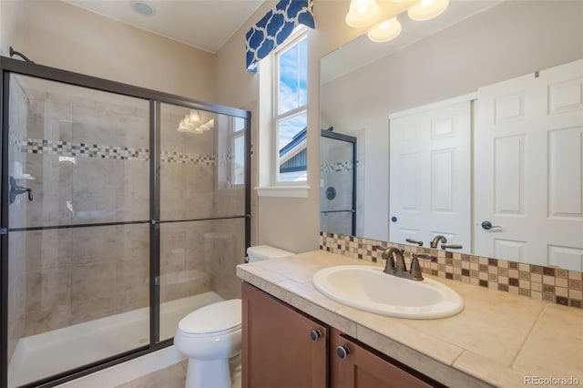 bathroom featuring backsplash, a shower with door, vanity, and toilet