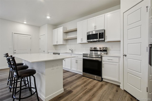 503 S Rollie Ave Unit 13C, Fort Lupton, CO 80621 - kitchen with appliances with stainless steel finishes, open shelves, a breakfast bar area, dark wood-type flooring, and a center island