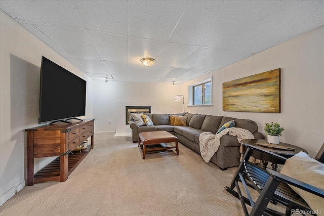 living area featuring light colored carpet, a glass covered fireplace, a paneled ceiling, and baseboards