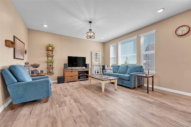 living room with a chandelier, a textured ceiling, and light hardwood / wood-style flooring