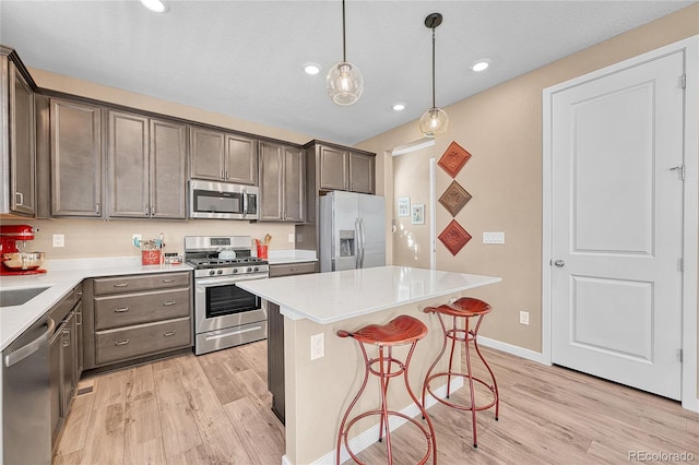 kitchen featuring pendant lighting, light wood-type flooring, appliances with stainless steel finishes, a kitchen island, and a kitchen bar