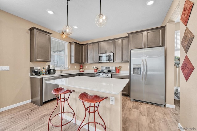 kitchen with stainless steel appliances, sink, pendant lighting, light hardwood / wood-style flooring, and a kitchen island