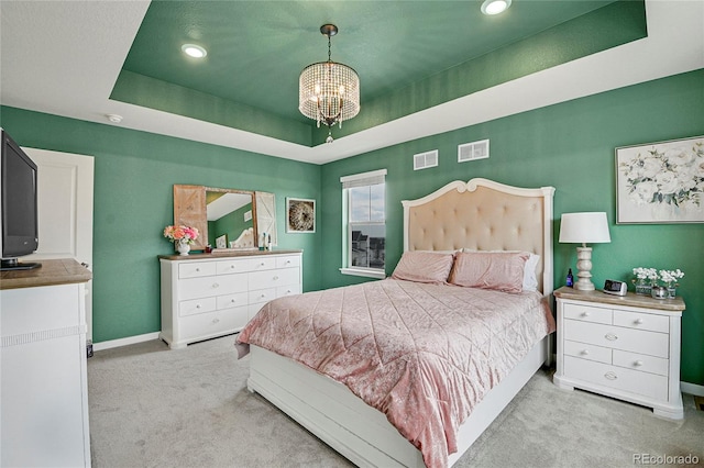 carpeted bedroom with a notable chandelier and a tray ceiling