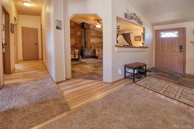 entrance foyer with a wood stove, wood walls, hardwood / wood-style floors, and ceiling fan