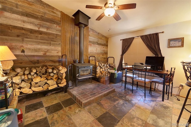 sitting room featuring a wood stove, wood walls, ceiling fan, and lofted ceiling