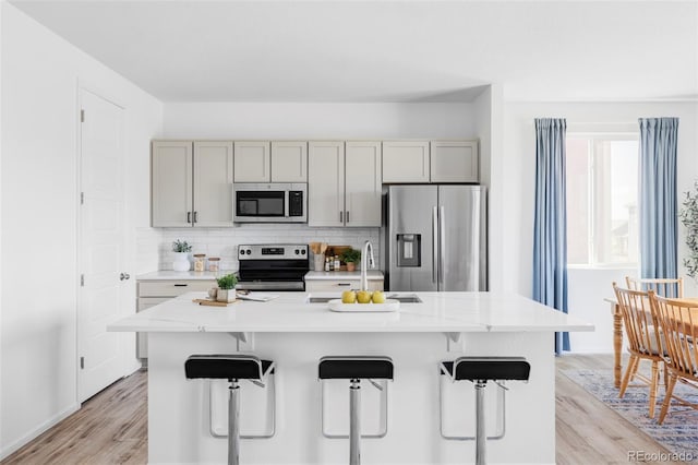 6117 Easton Cir, Frederick, CO 80504 - kitchen with appliances with stainless steel finishes, light wood finished floors, tasteful backsplash, a breakfast bar area, and gray cabinets