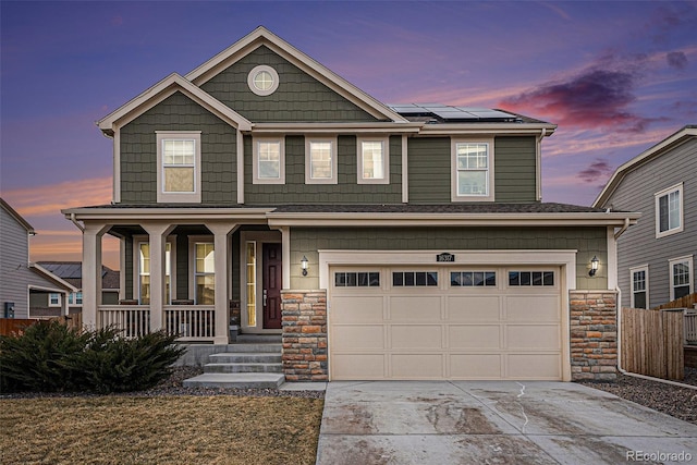 craftsman inspired home featuring a porch, a garage, solar panels, concrete driveway, and stone siding