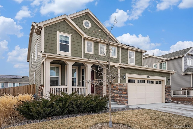 view of front of home featuring a porch, stone siding, driveway, and fence