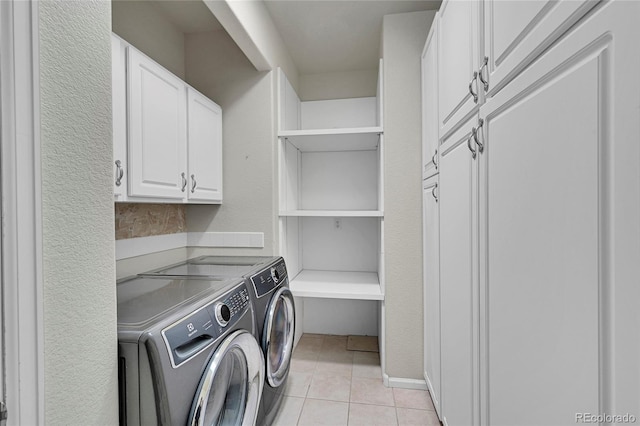 clothes washing area with cabinets, washing machine and clothes dryer, and light tile patterned floors