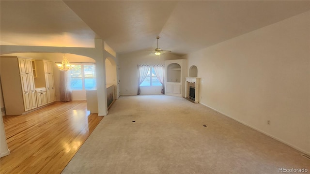 unfurnished living room featuring ceiling fan with notable chandelier, vaulted ceiling, built in shelves, and light wood-type flooring